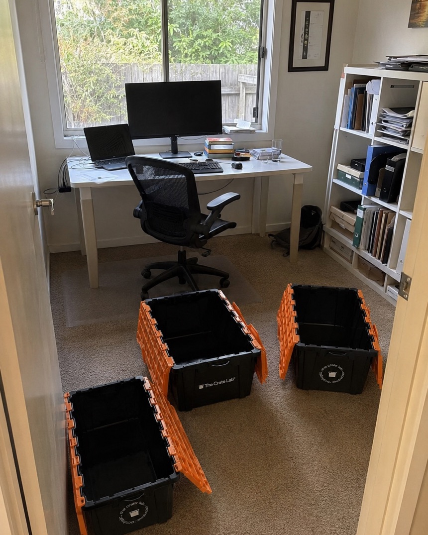 A home office desk cluttered before a move, empty Crate Lab crates waiting